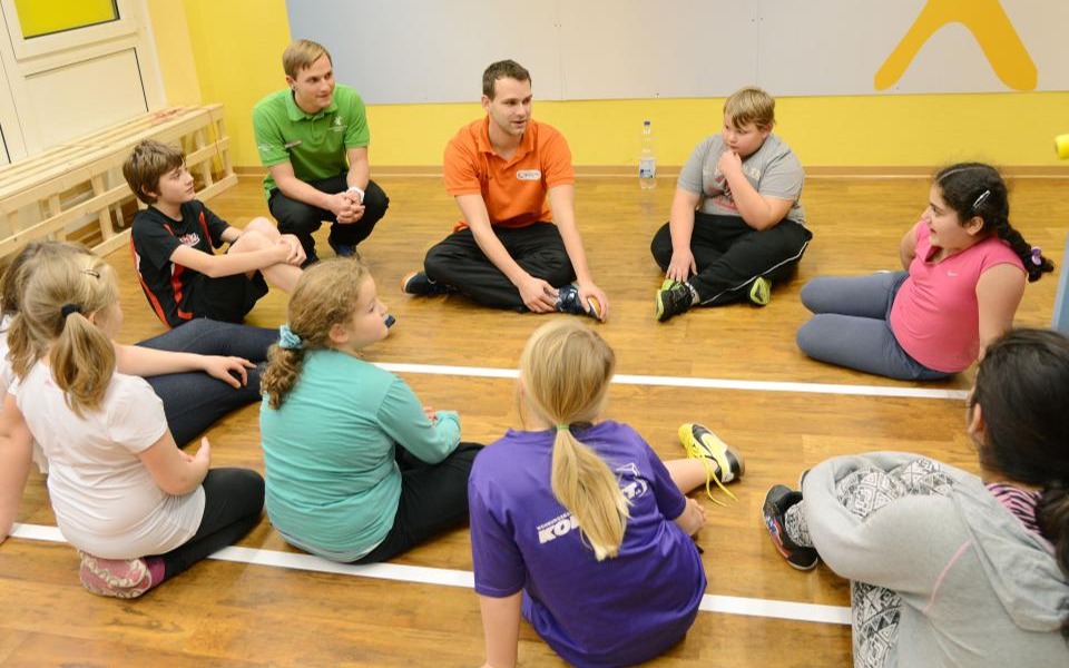 Kinder sitzen im Kreis mit Trainern